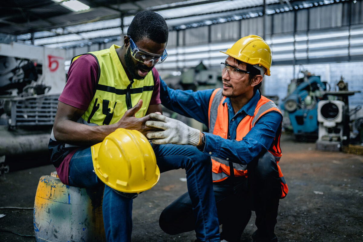 A supervisor kneeling next to a worker to assist with a safety concern and possible injury in the workplace.