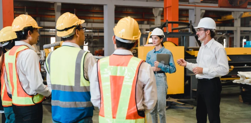 Industrial team conducting a workplace safety meeting on the job site with workers wearing PPE and high-visibility vests.