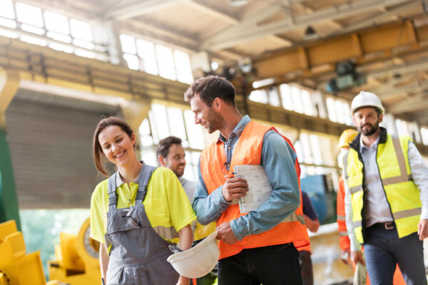 Industrial safety team walking through a factory floor in high-visibility gear, smiling and engaged in conversation