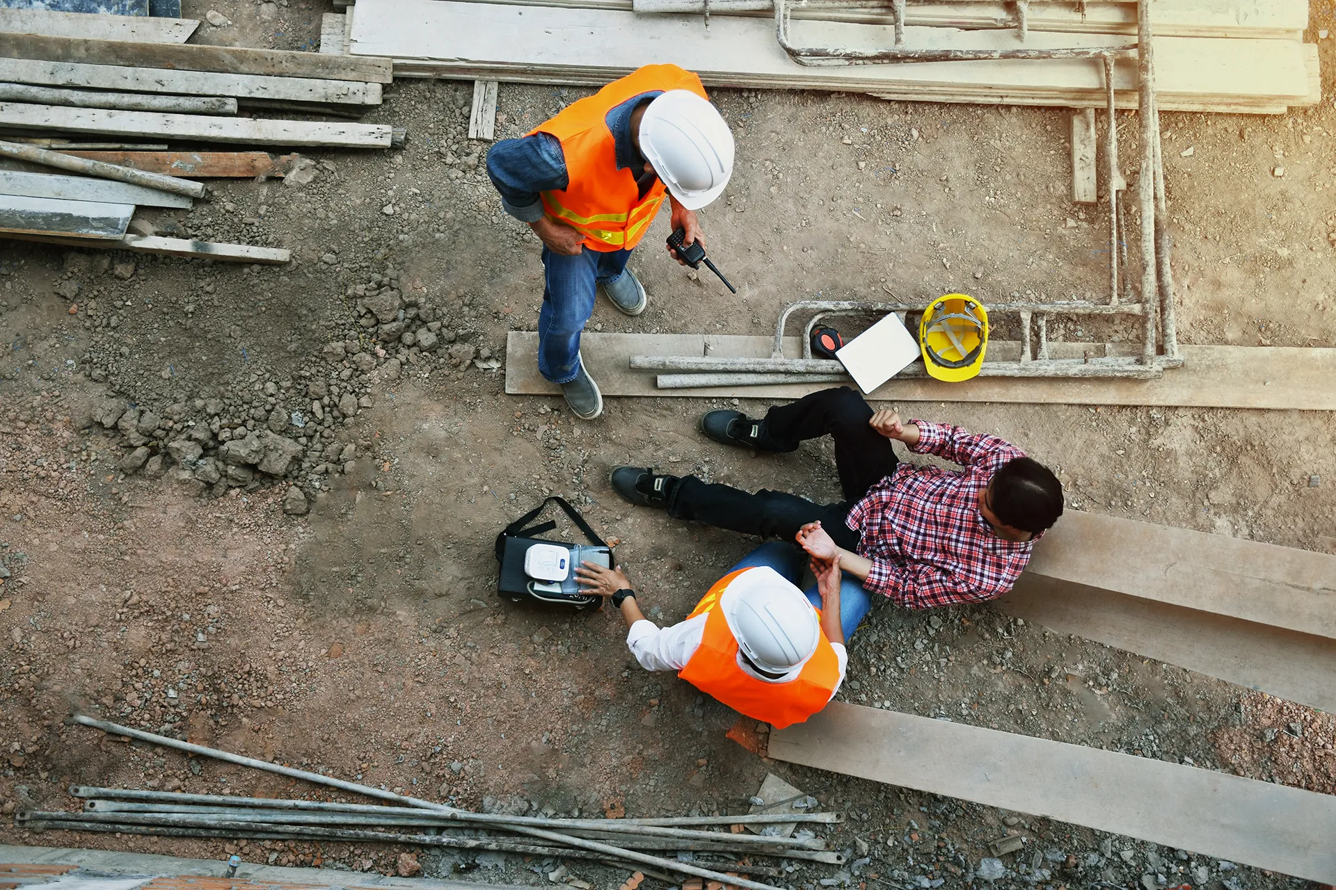 Construction workers in orange vests and hard hats discuss at a construction site with tools and wooden planks.
