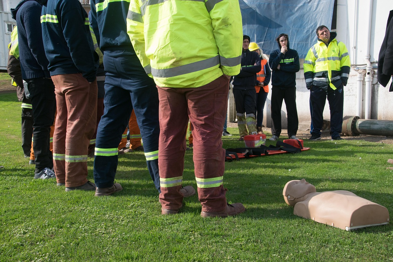 First aid attendants in high-visibility workwear participate in workplace emergency response training with a CPR mannequin on site.